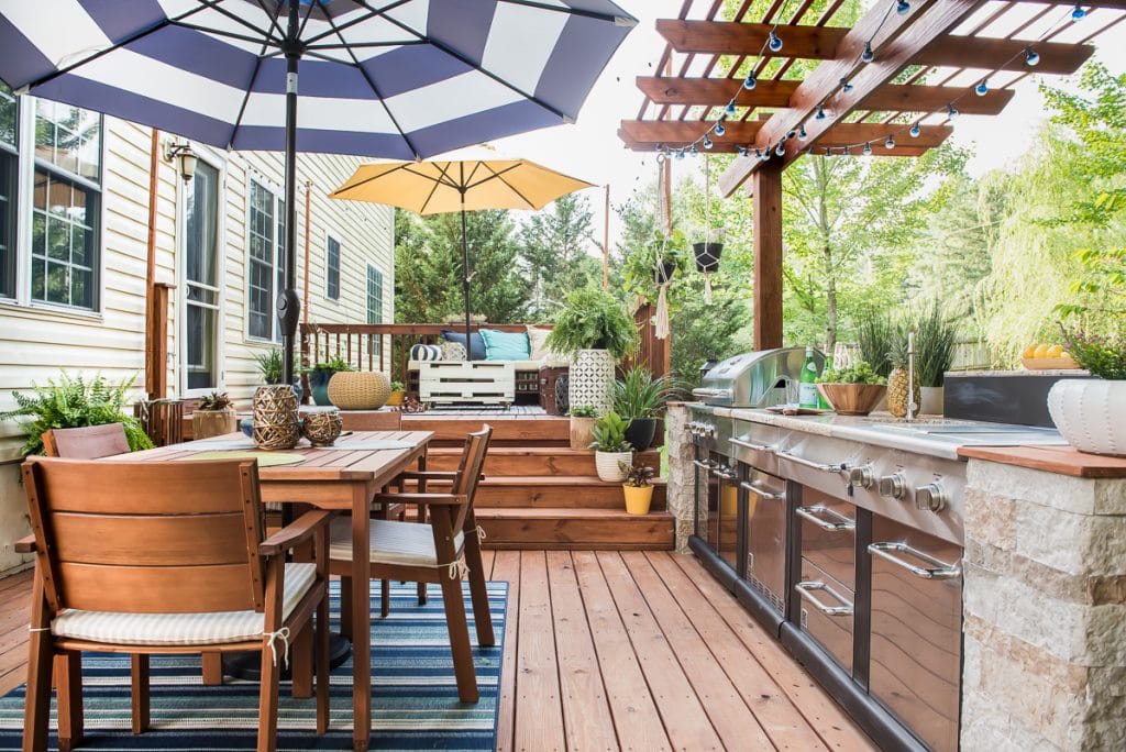 Stunning Outdoor Kitchen Makeover with white and blue umbrella and wooden table.