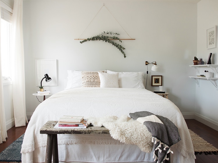 sprigs of eucalyptus hang on the wall above a bed