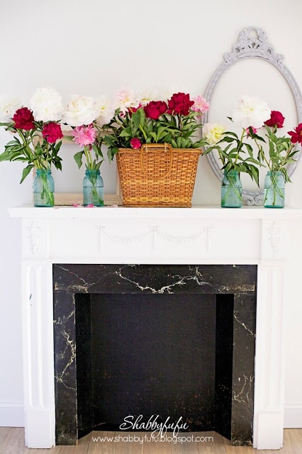 white fireplace with a basket of flowers and jars filled with flowers on the sides