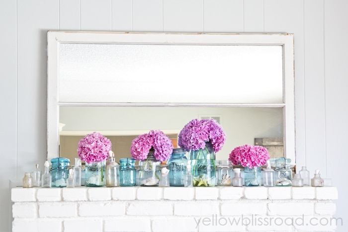 bright pink blooms and blue jars in front of a mirror on a mantel