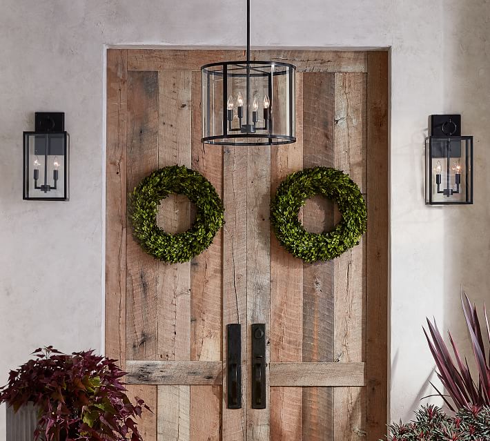 Wooden door with green wreaths on it and a bronze farmhouse entryway light hanging from the ceiling