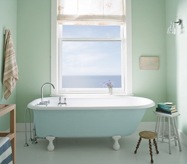 Sunny bathroom with walls painted in Palladian Blue by Benjamin Moore, with a pale blue clawfoot bathtub.