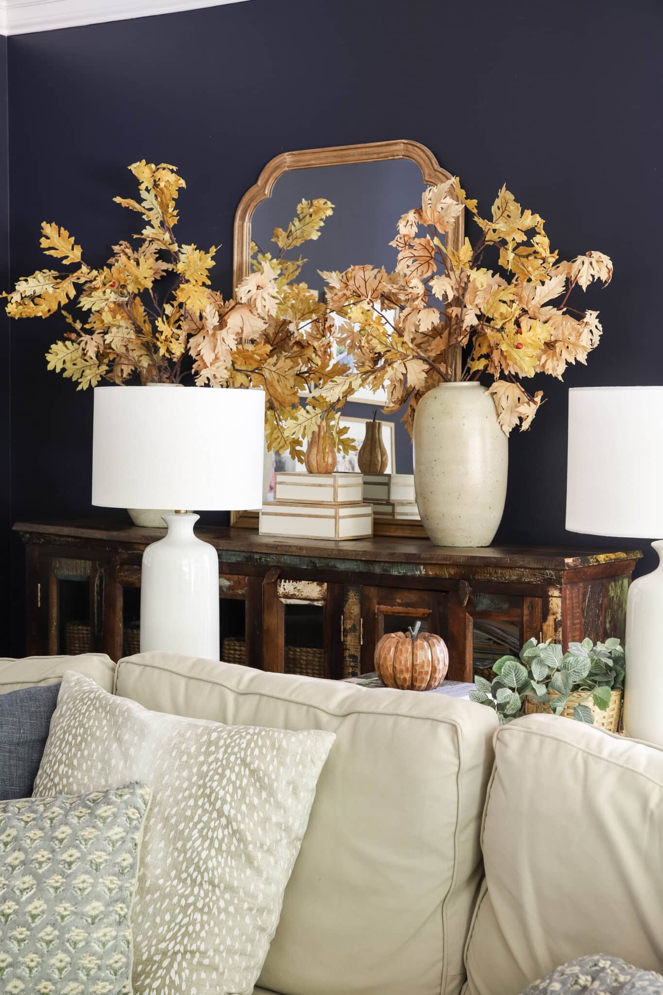 leafy autumn oak stems in earthen vases in a living room with navy walls.