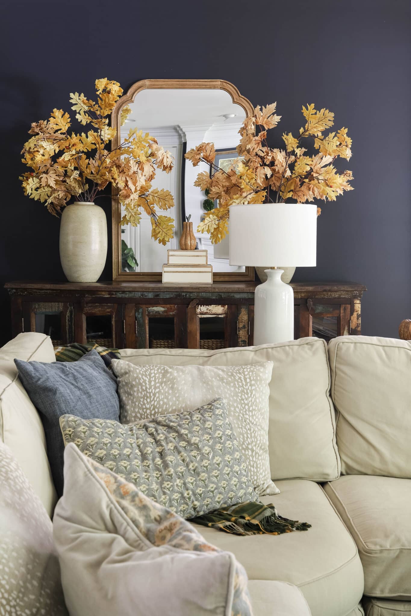 fall throw pillows on a sectional sofa with navy walls in a living room.