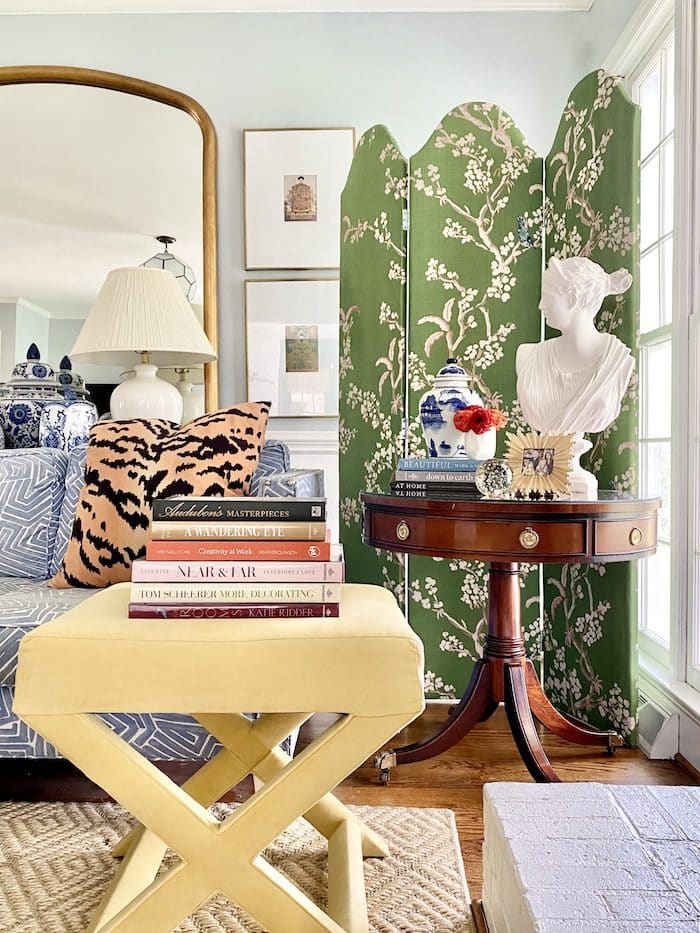 living room with a folding screen in the corner, a lady bust statue and a side table with books and other decor.