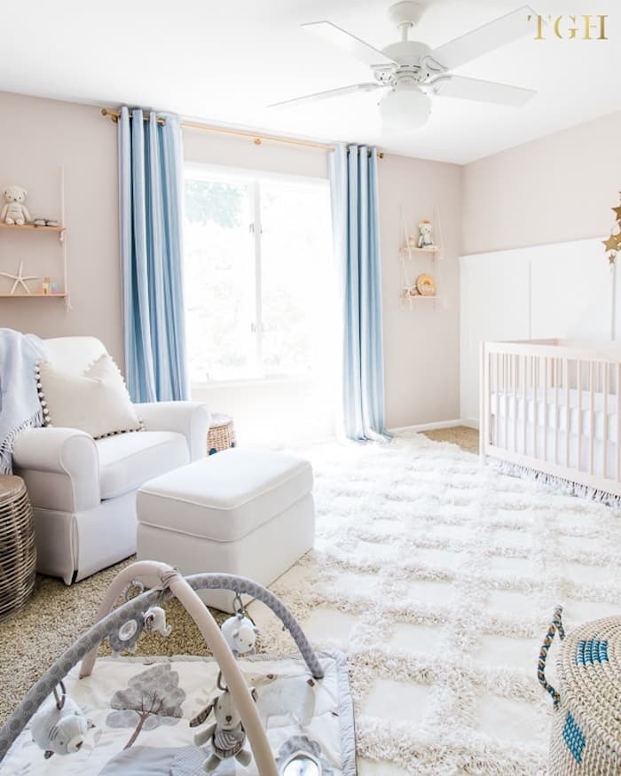 neutral beige nursery with blue curtains and comfortable white rug.