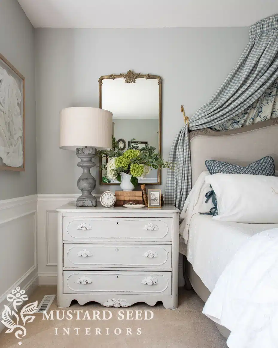 Primary bedroom with gray walls, fabric valance over the bed, antique painted dresser and an antique mirror.