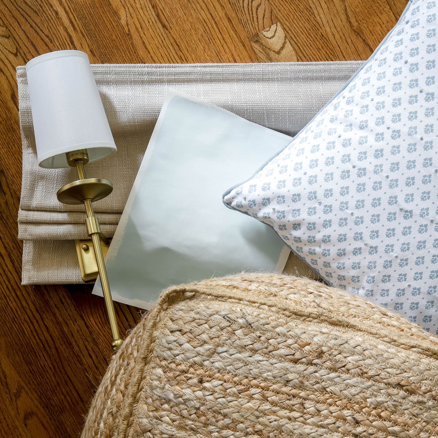 brass sconce, light blue green paint swatch, blue and while pillow and jute pouf for decor.
