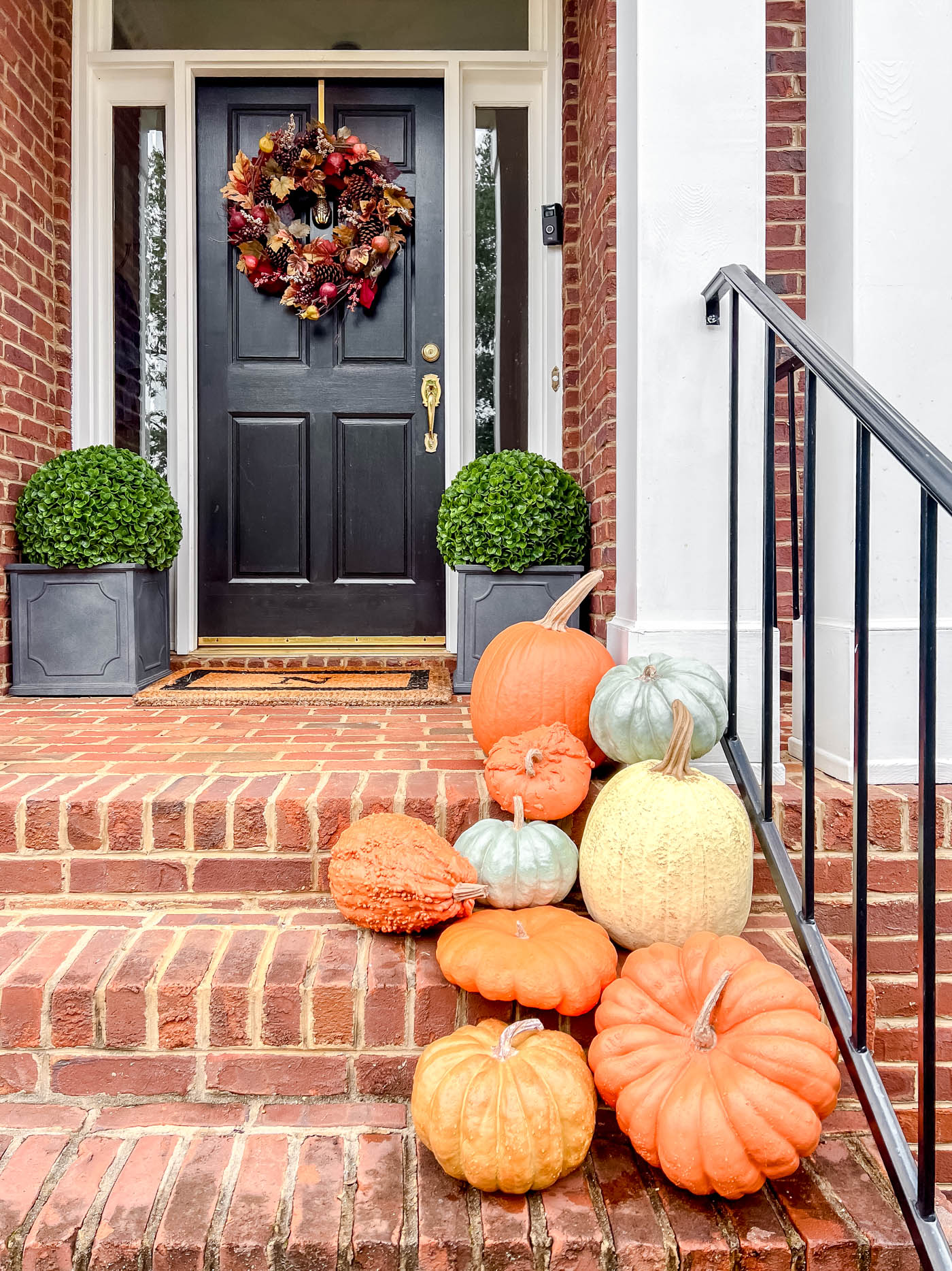 faux pumpkins on a front porch with autumn wreath.