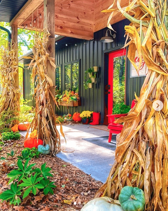 pretty front porch for fall with hay stalks and pumpkins with a red door.