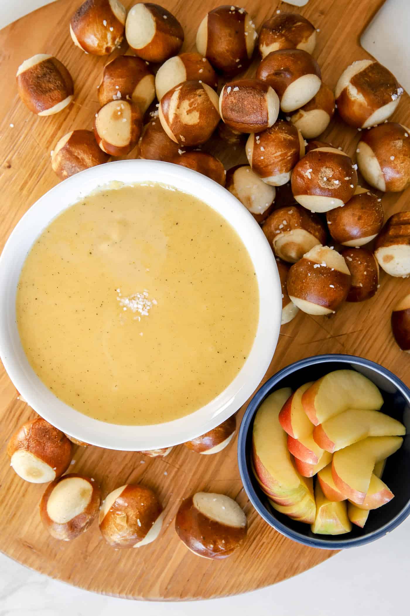 serving beer cheese pretzel dip on a charcuterie board with pretzel balls and apple slices.