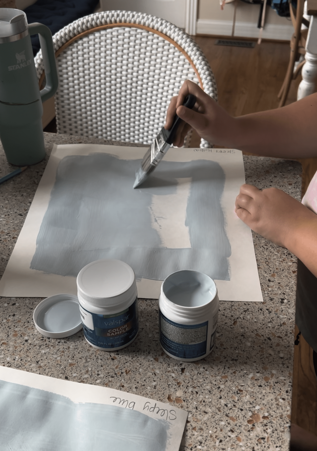 painting a blue paint swatch on a poster board.