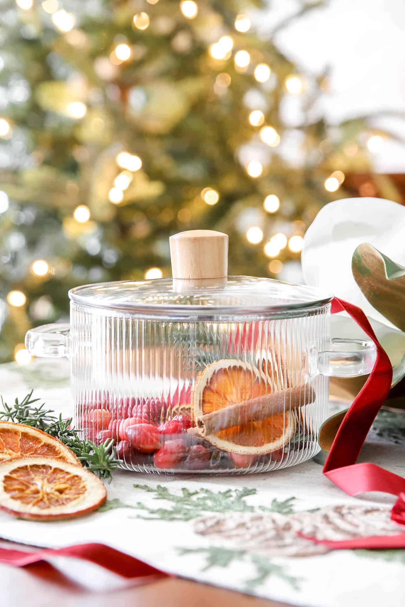 rosemary, oranges and cinnamon in a clear pot in front of a Christmas tree.