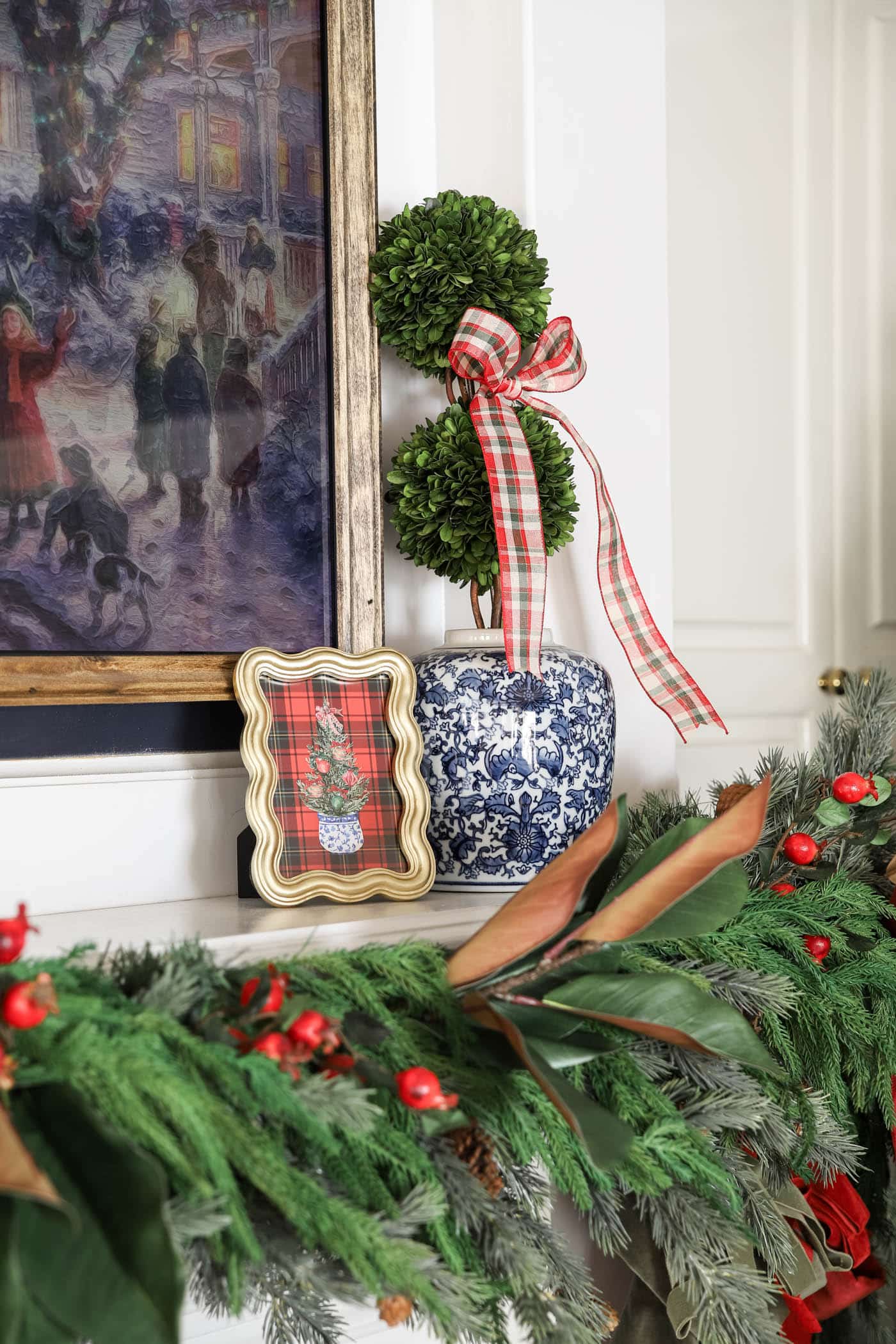 chinoiserie pot with boxwood and ribbon next to plaid christmas art.