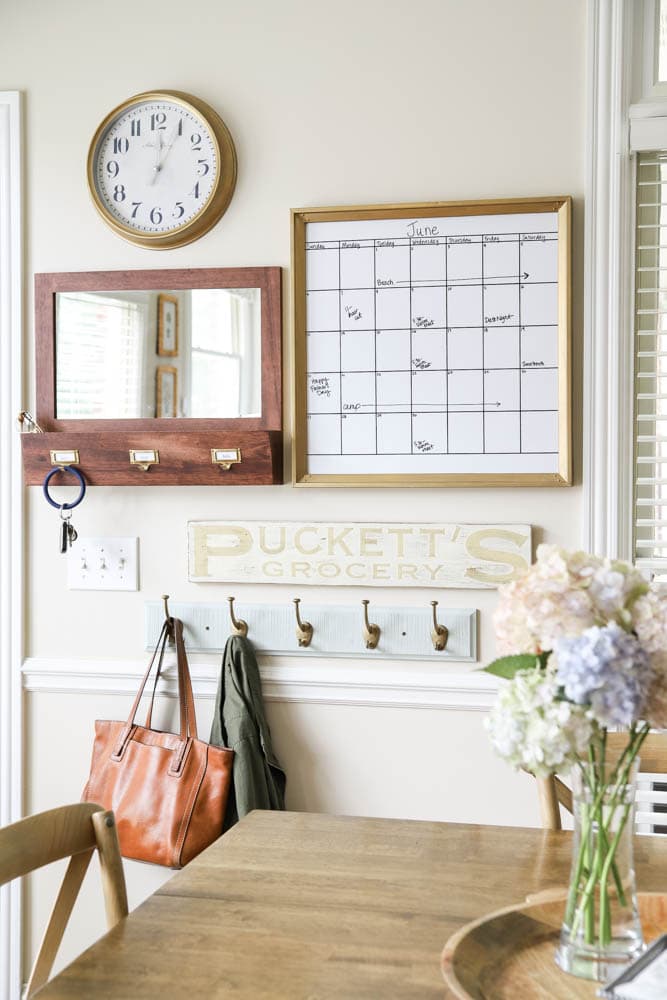 calendar, mirror, mail sorter and hooks in the entry way of a kitchen area.