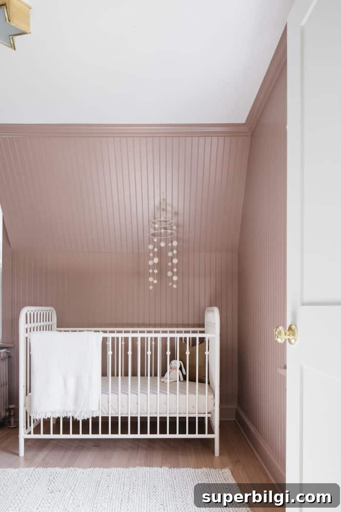 20 Nursery Paint Colors and Accent Wall Ideas for Baby Rooms 8 Seaside Sand (pink) walls with beaboard and a white crib with a mobile hanging over it.