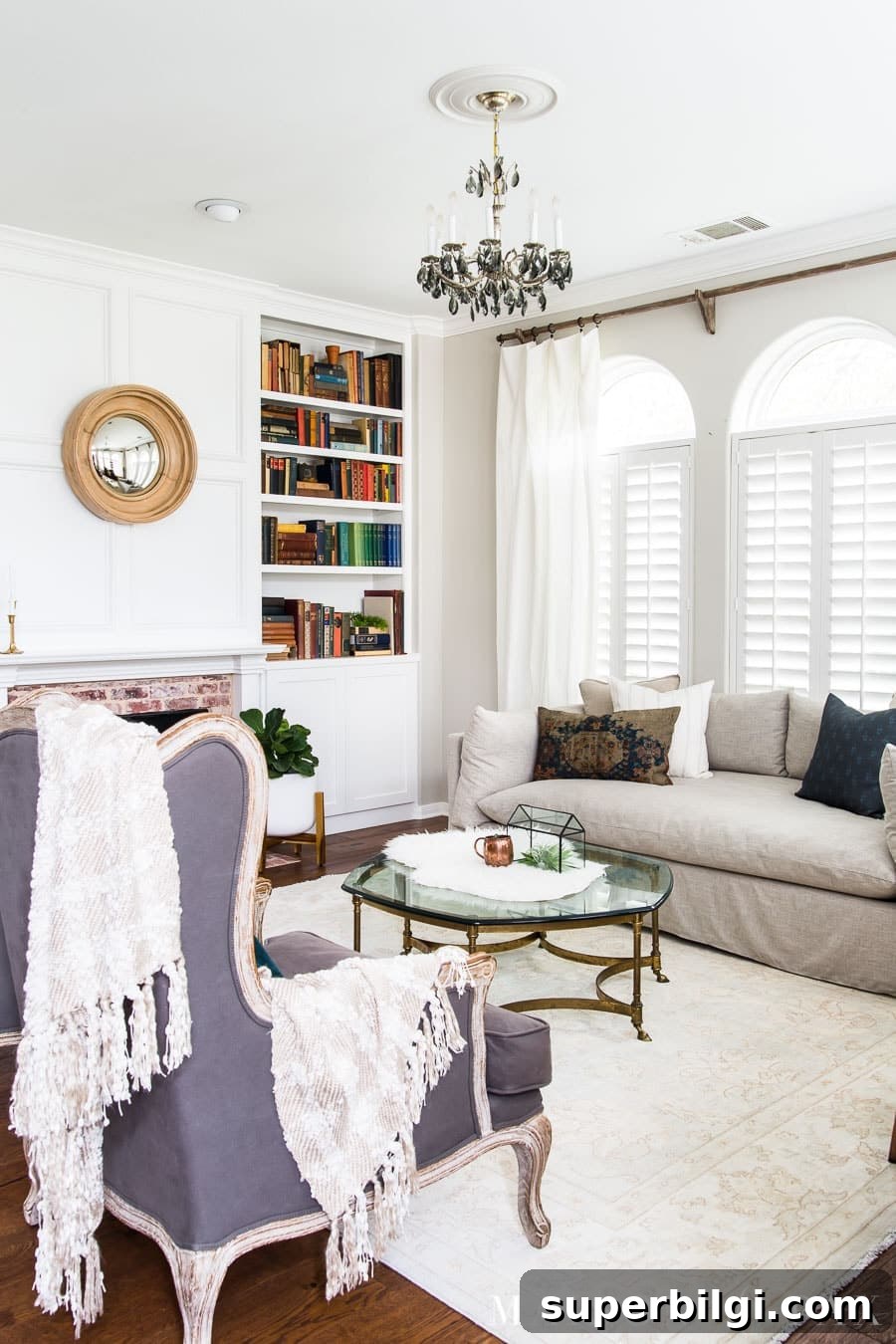 Paint Trim Like a Pro: Step-by-Step Guide 4 Neutral transitional living room with a slipcovered sofa, built-in bookshelves, white fireplace, glass coffee table, and arched windows with plantation shutters.