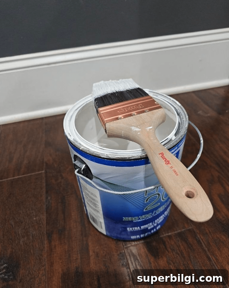Paint Trim Like a Pro: Step-by-Step Guide 5 Paintbrush resting on an open can of white paint on a hardwood floor before painting a room.