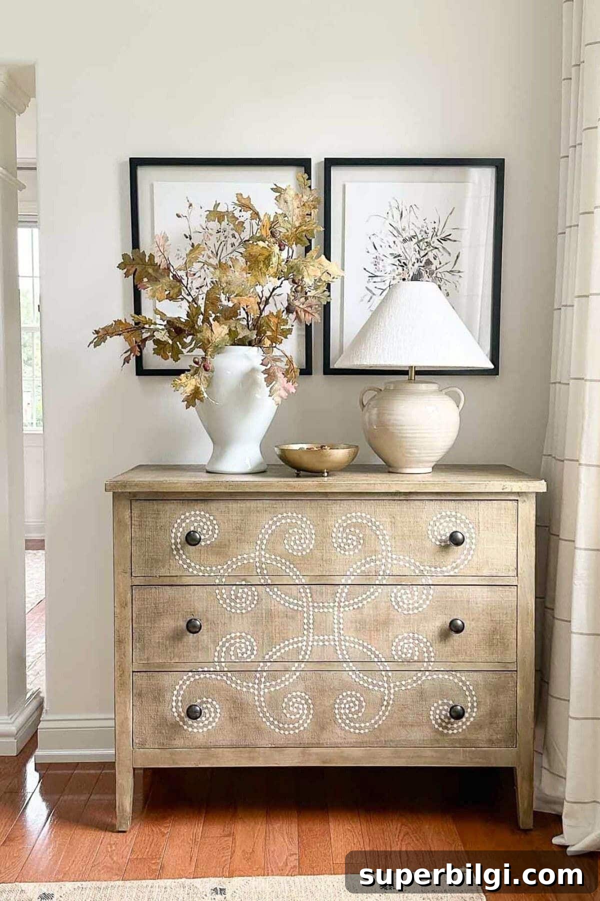 light wood dresser with fall foliage in a vase and a lamp.
