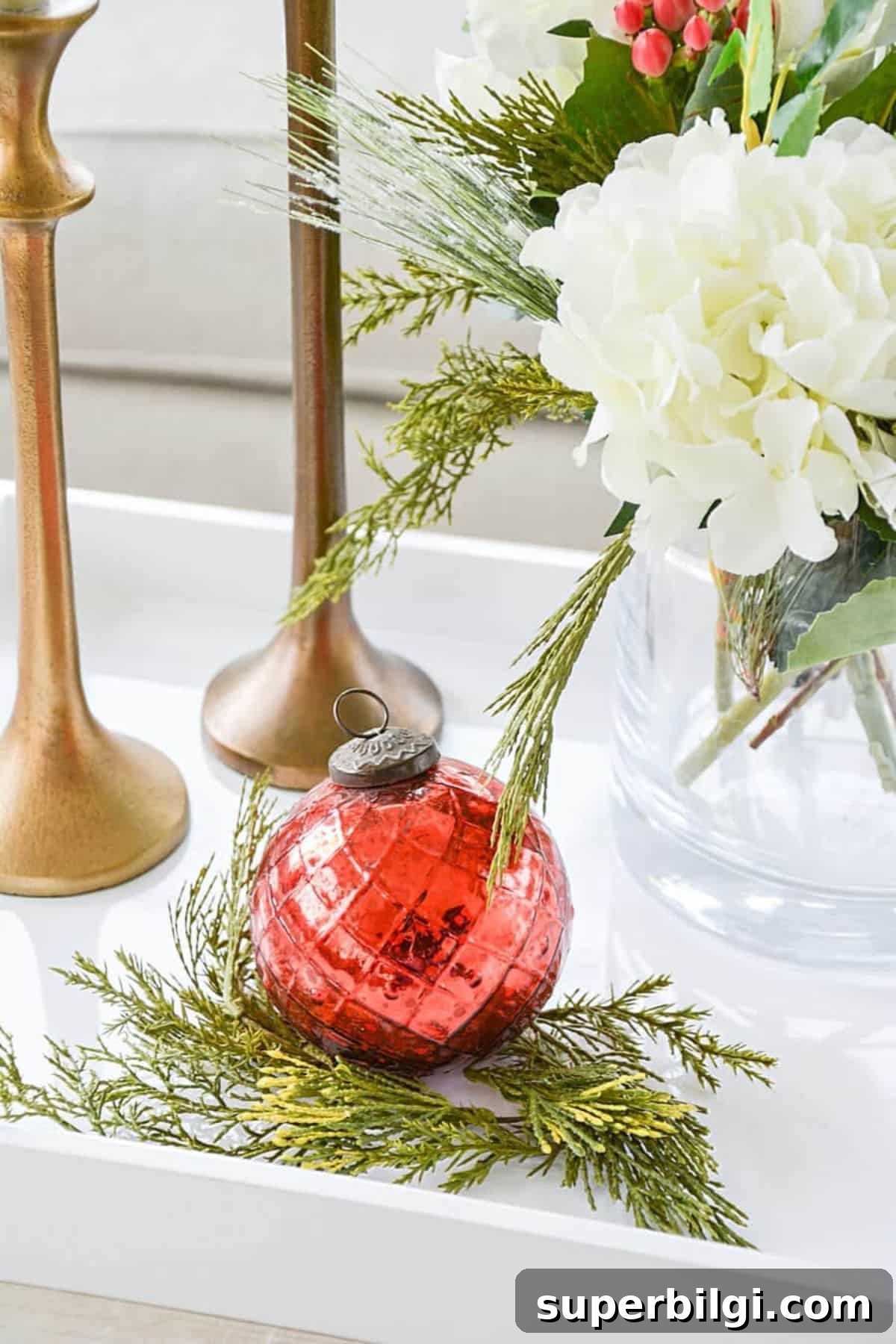 red ornament on some greenery next to flowers and candlesticks.