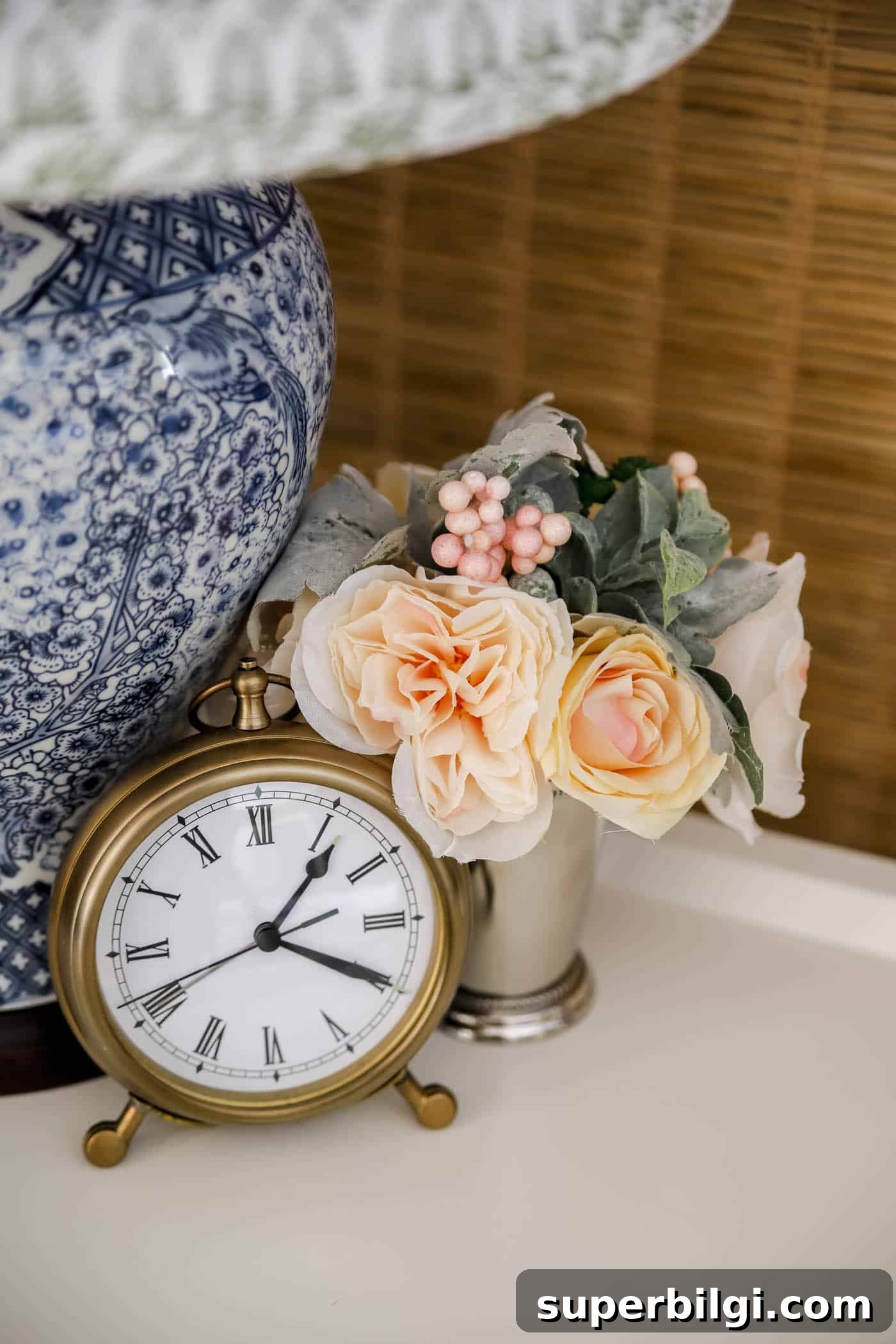 Spring Bedroom Decor Ideas to Instantly Refresh Your Space 8 small bouquet of faux flowers in a mint julep cup, along with a pocket watch clock and blue and white lamp vase on a nightstand.